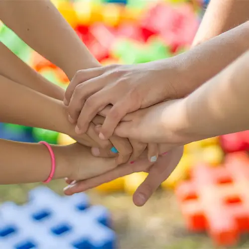 Mehrere Hände von Erwachsenen und Kindern, die aufeinandergelegt sind. 