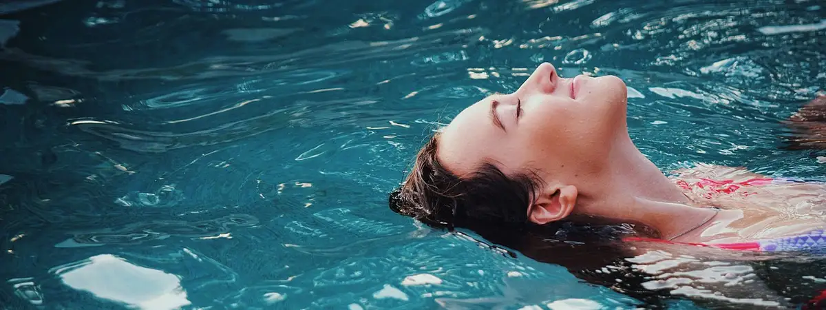 Ein Foto einer Frau, die entspannt auf dem Rücken im Wasser treibt, mit geschlossenen Augen und einem friedlichen Gesichtsausdruck.